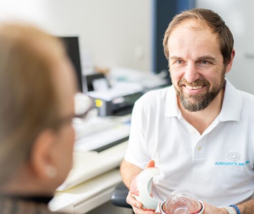 Herr Witschel führt ein Aufklärungsgespräch mit einem Patienten und lächelt dabei freundlich